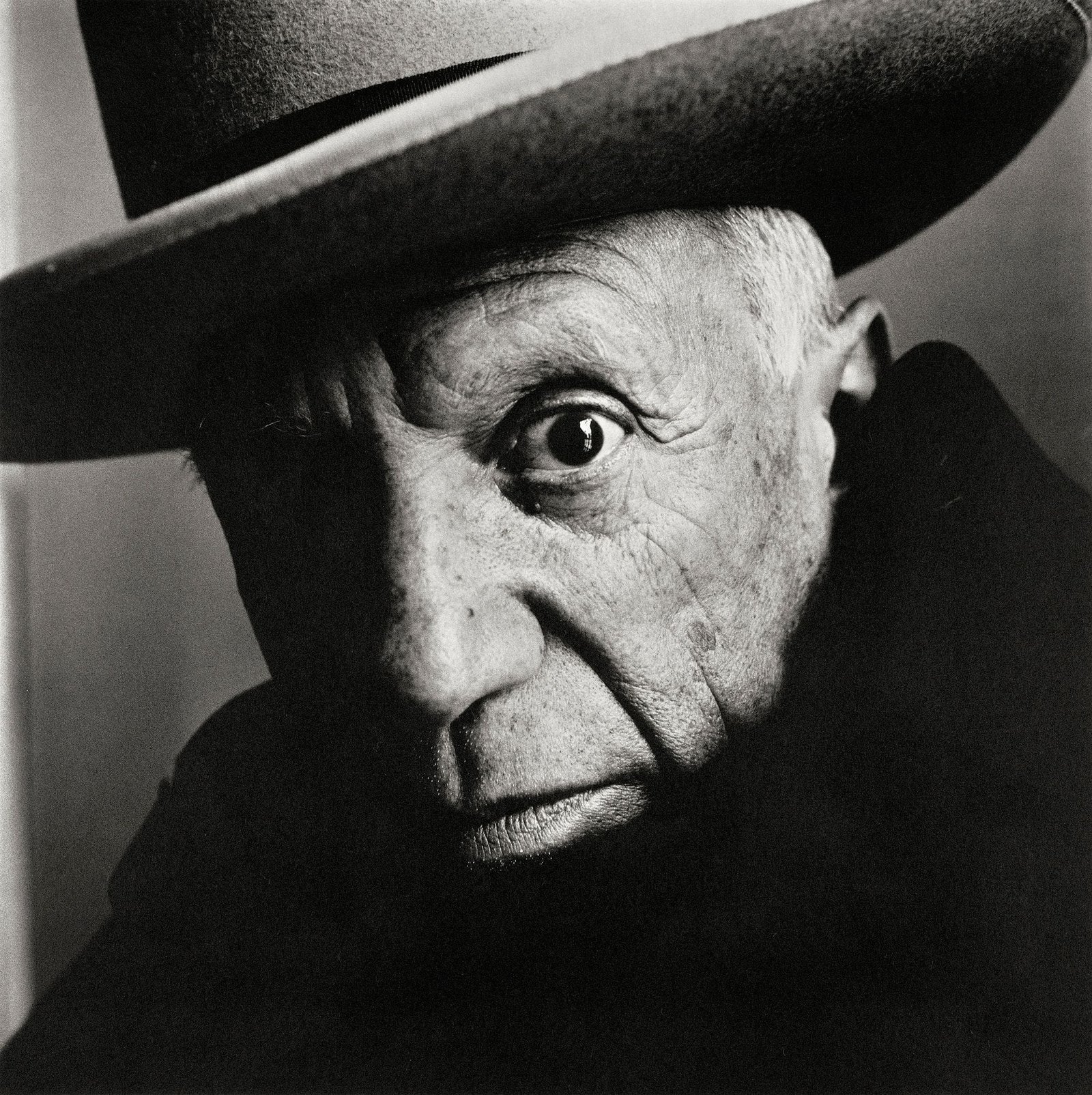 Picasso with intense gaze wearing a dark hat, portrayed in a high-contrast black and white image.