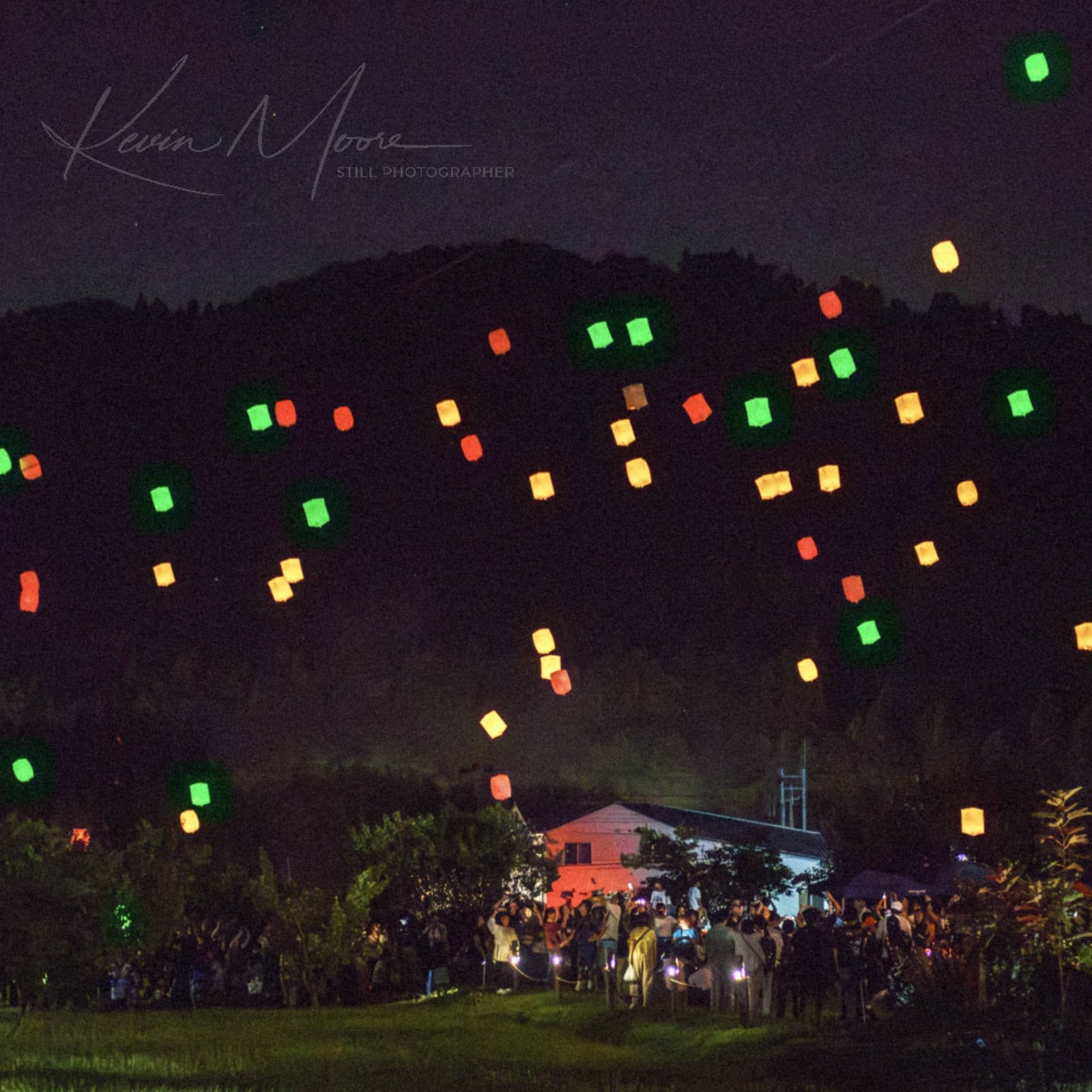 Lantern festival at twilight with crowd releasing colorful lanterns into night sky.