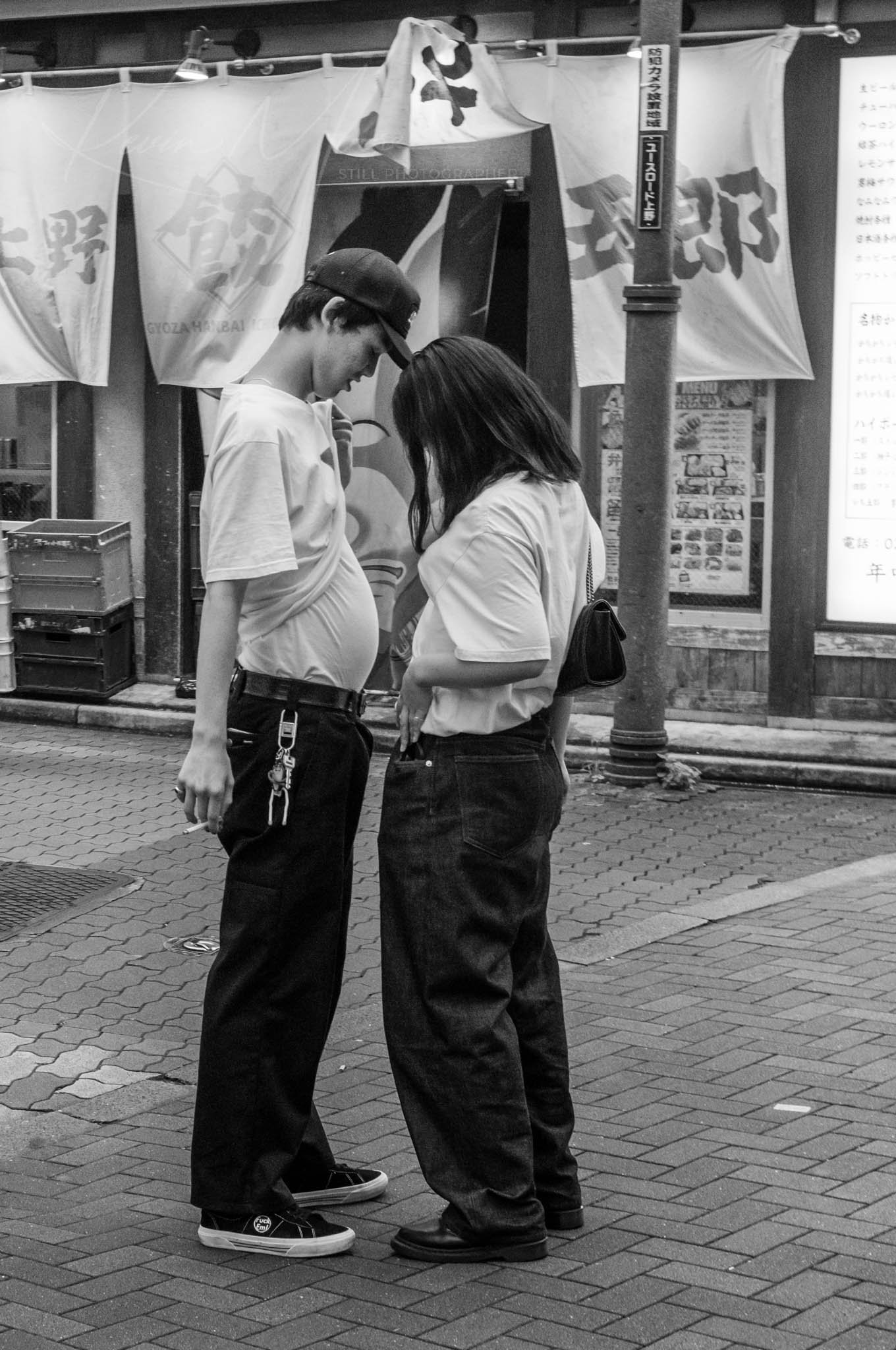 Young couple intimately converses on a bustling city Ueno Tokyo street in black and white photo.