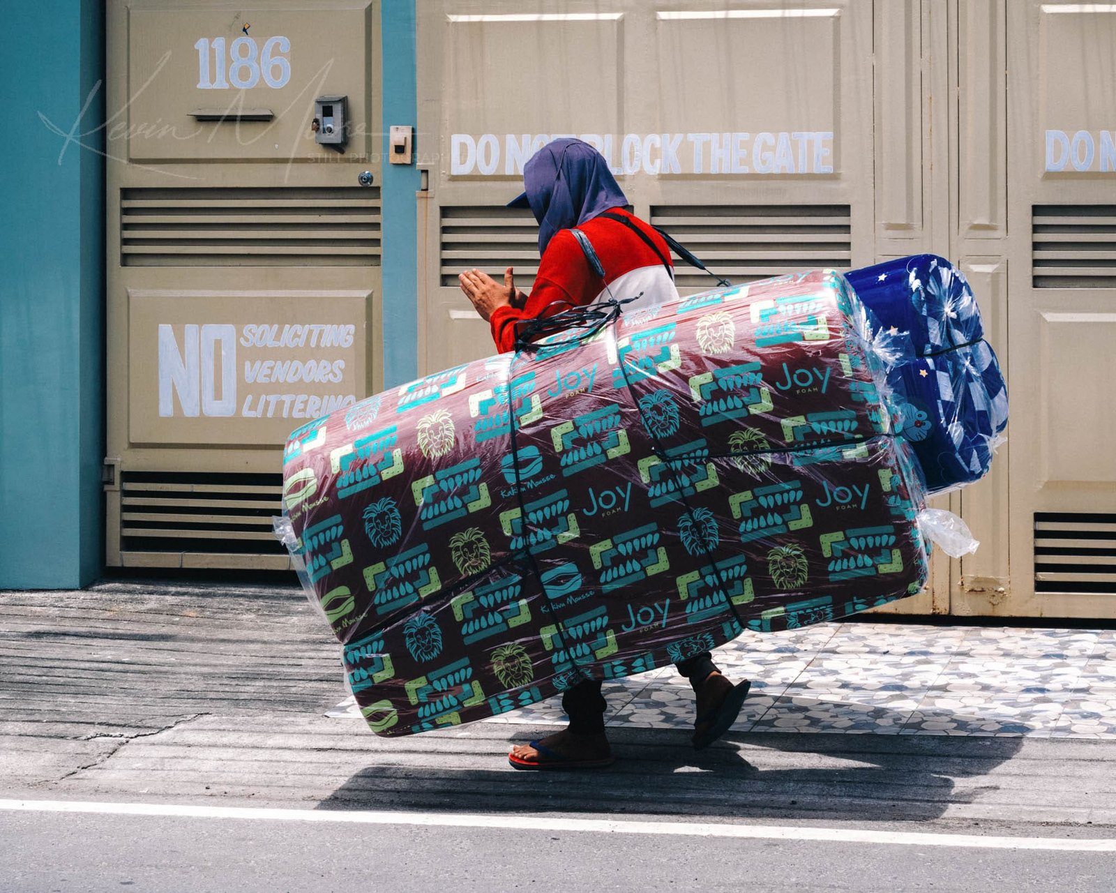 Man selling mattresses on busy street with colorful cargo.