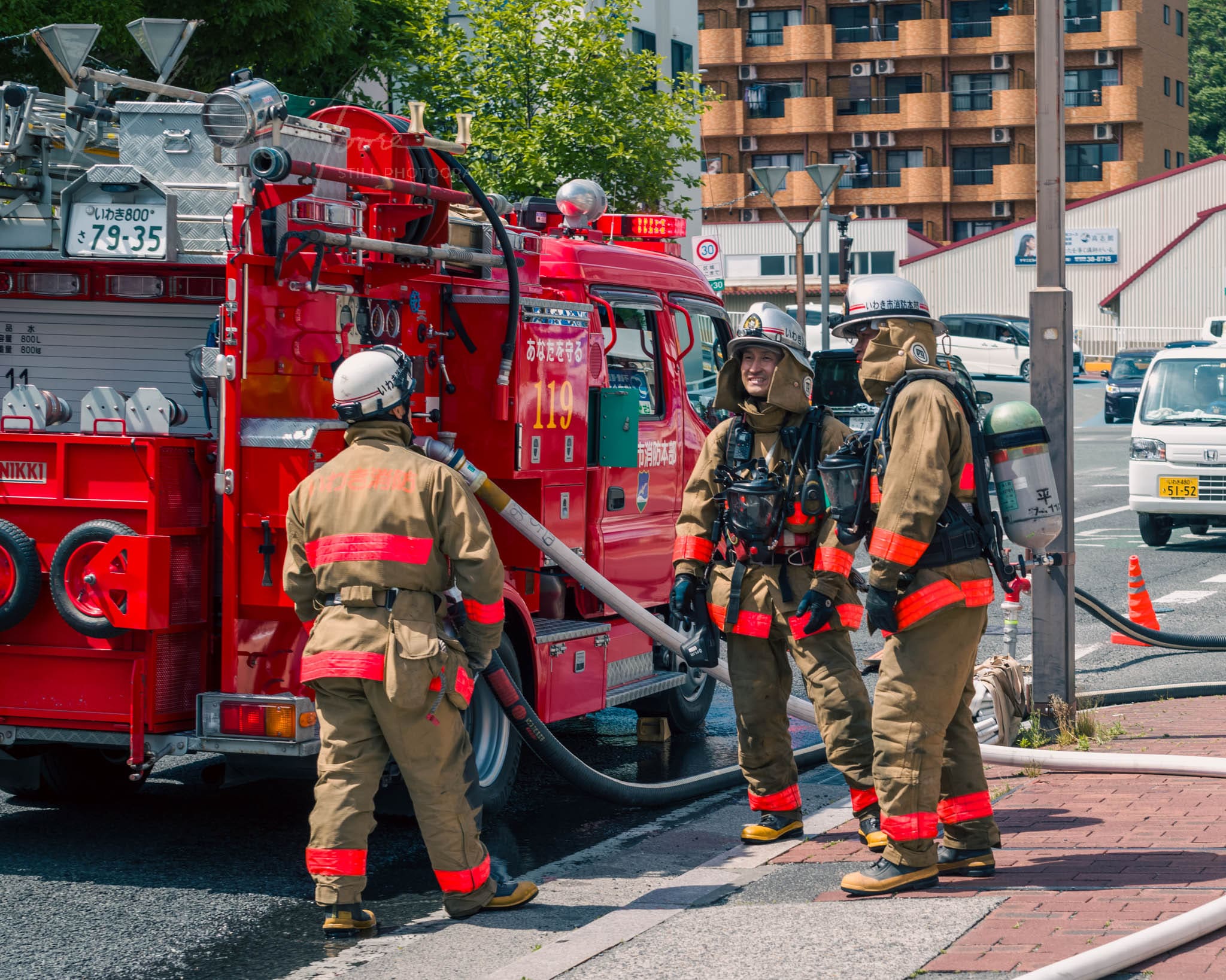 Japanese Firefighters in action with hose and engine 119 on sunny day.