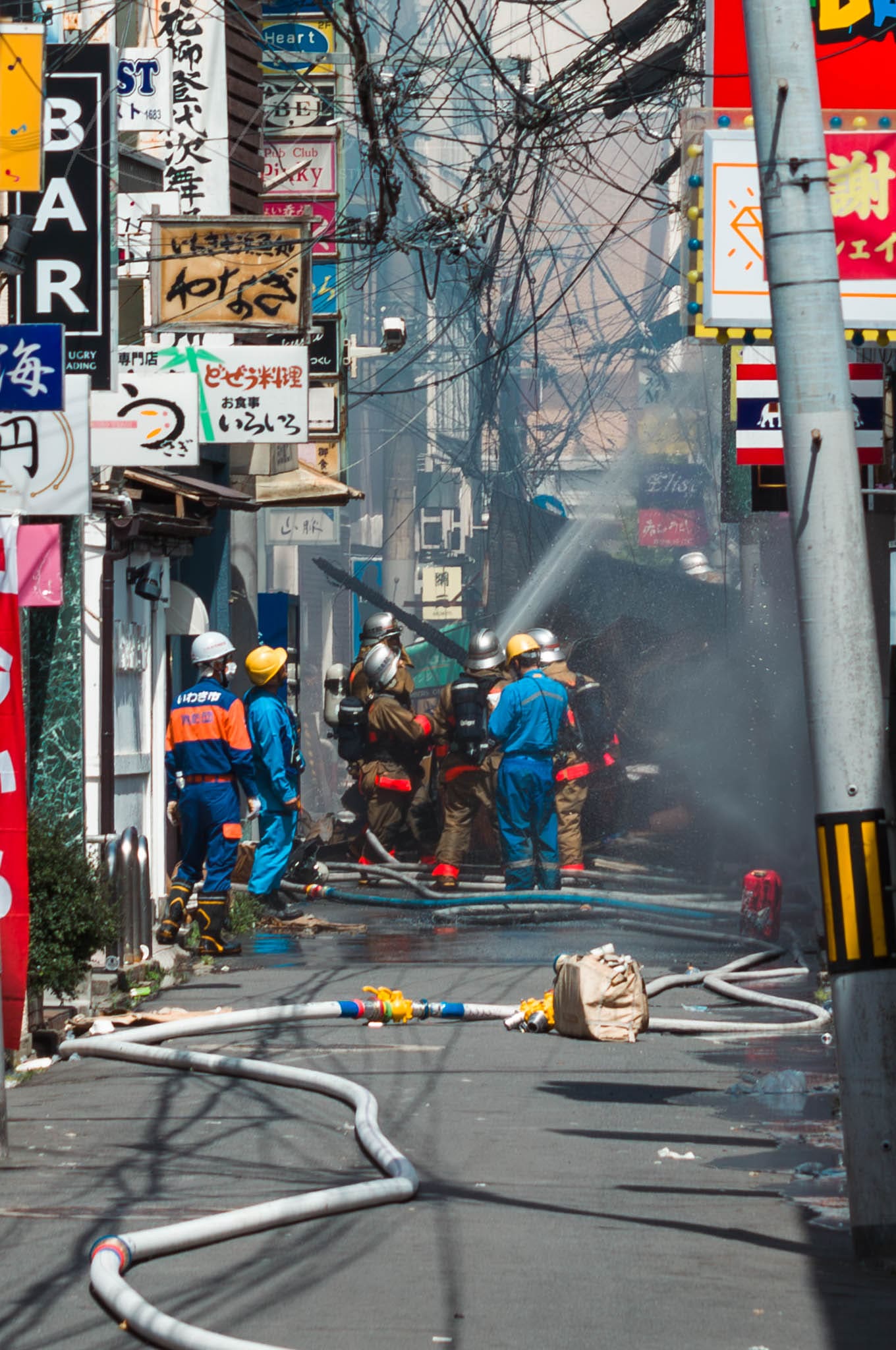 Japanese Firefighters battle intense blaze in urban setting under tangled wires.