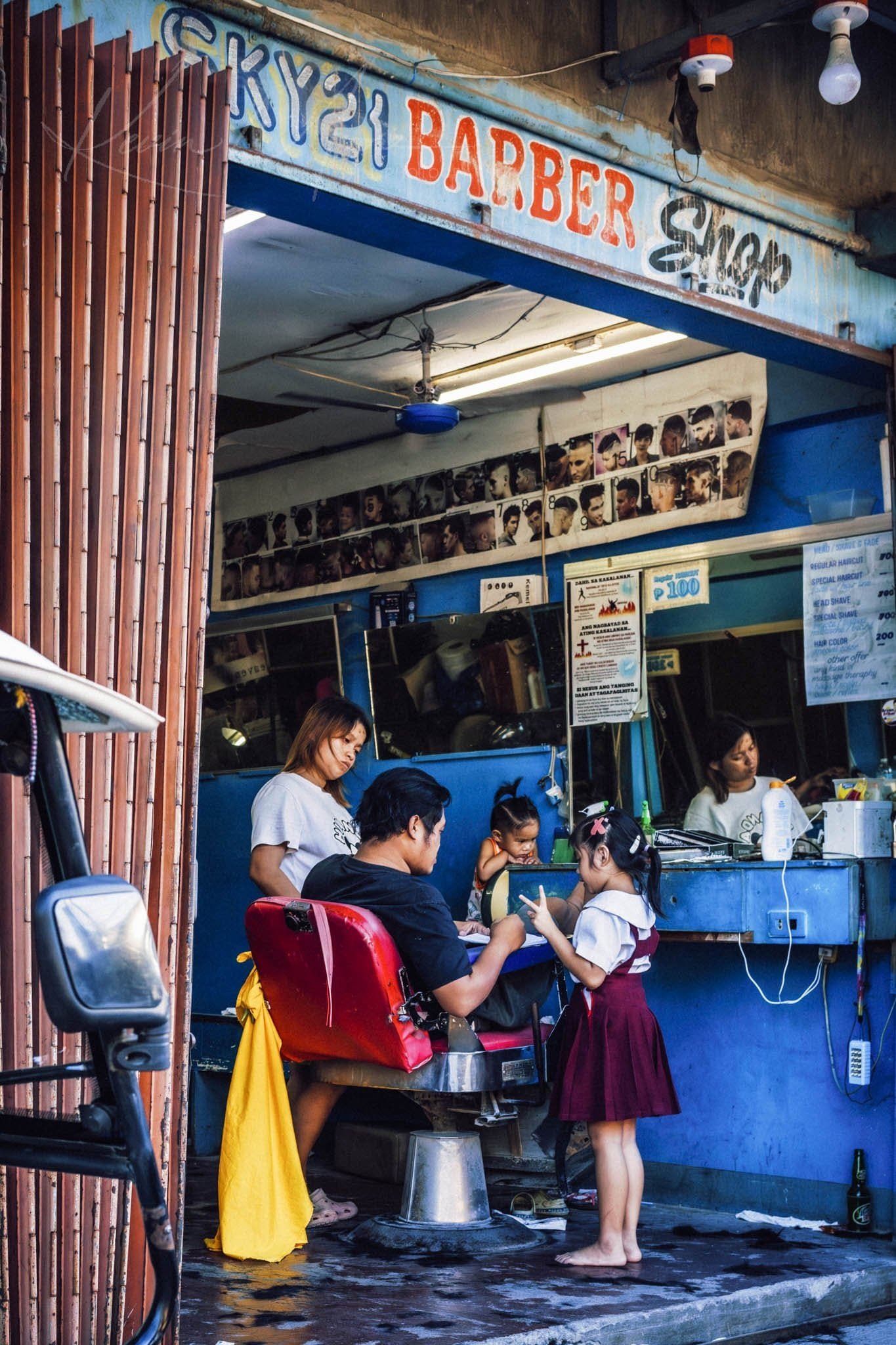 Barber attentively cuts hair of child in vibrant Philippines barber shop.